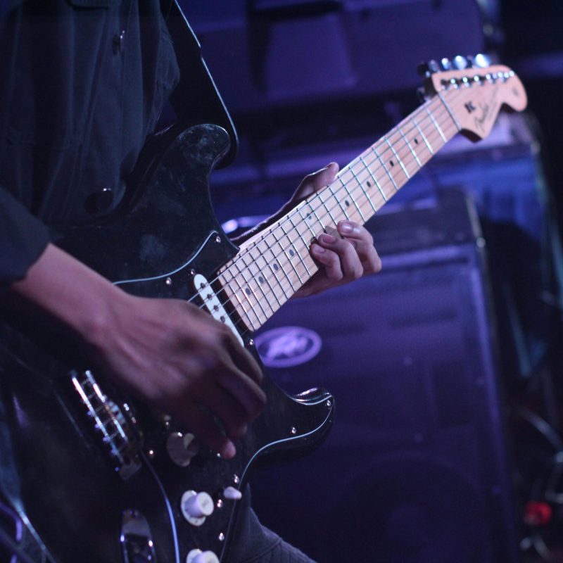 Musician playing an electric guitar on stage during a live performance.